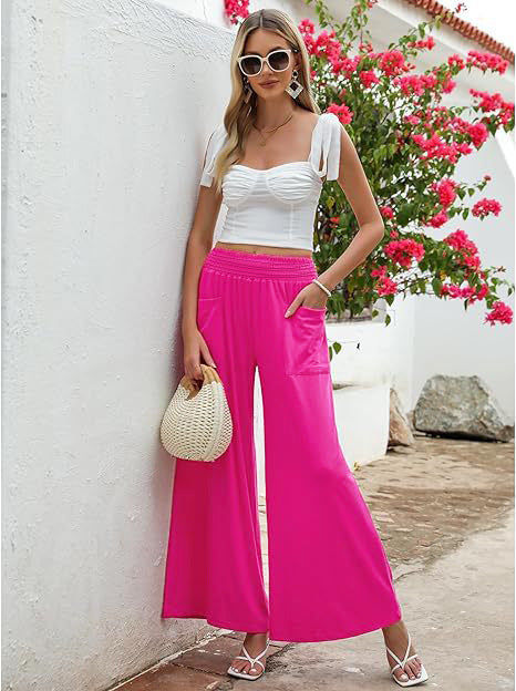 Woman in white top and pink pants standing against a white wall with pink flowers.