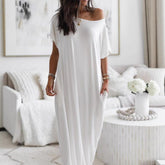 Woman wearing a white off-shoulder dress in a bright living room.
