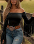 Woman wearing a black off-shoulder top with fringe, blue jeans, and a brown belt with a large buckle.