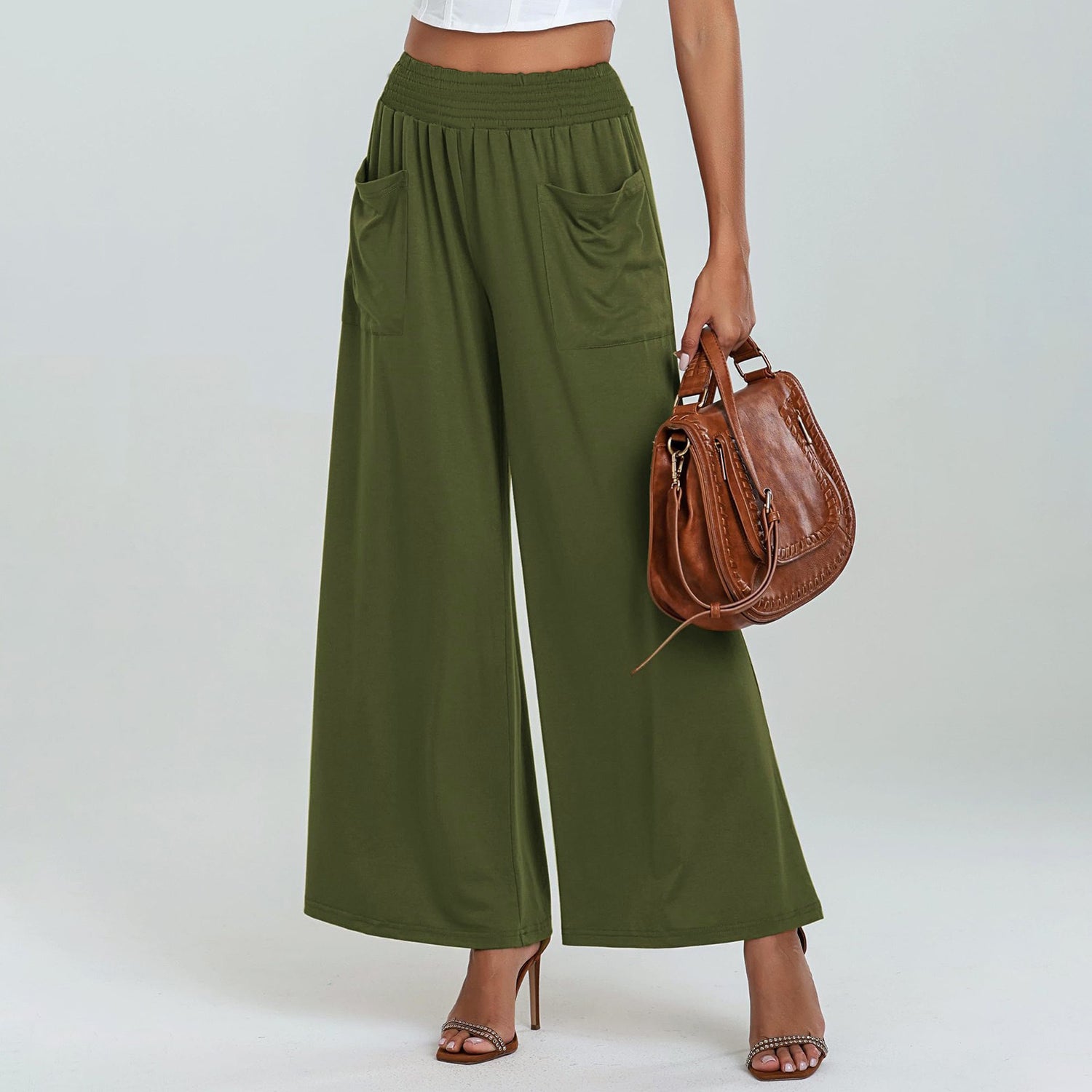 Person wearing green wide-leg pants holding a brown handbag on a white background