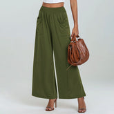 Person wearing green wide-leg pants holding a brown handbag on a white background