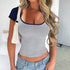 Woman wearing a gray tank top with navy trim and blue jeans, holding a white bag.