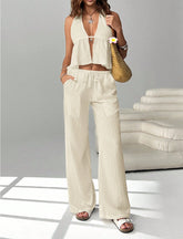 Woman in a white sleeveless top and beige wide-leg pants holding a woven bag.