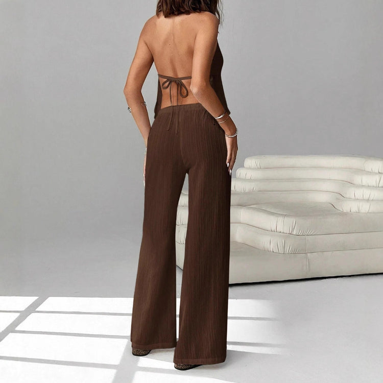 Person wearing a brown outfit with wide-leg pants and a backless top in a minimalistic setting.