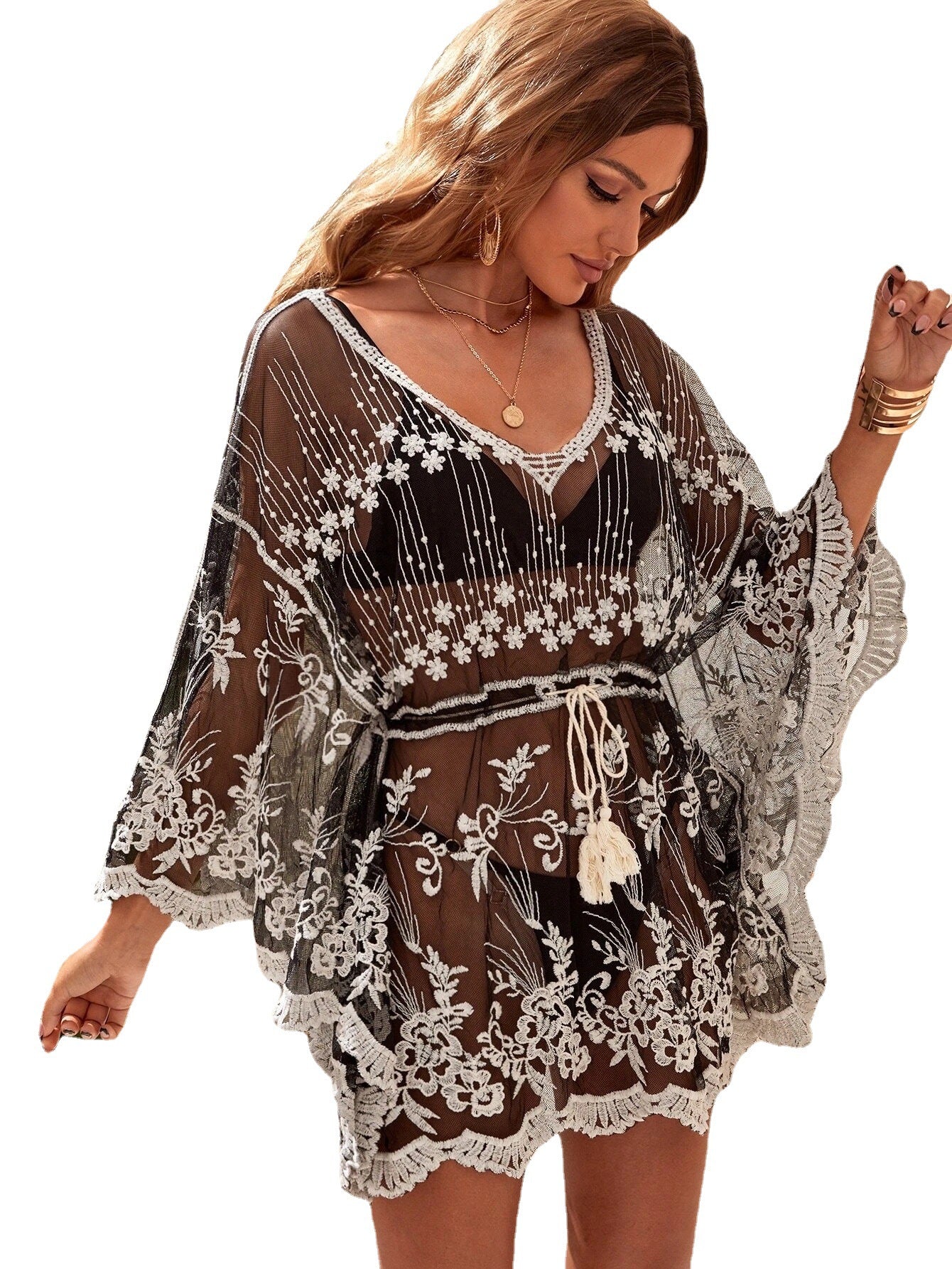 Woman wearing a black and white embroidered dress with sheer sleeves on a white background