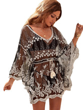 Woman wearing a black and white embroidered dress with sheer sleeves on a white background